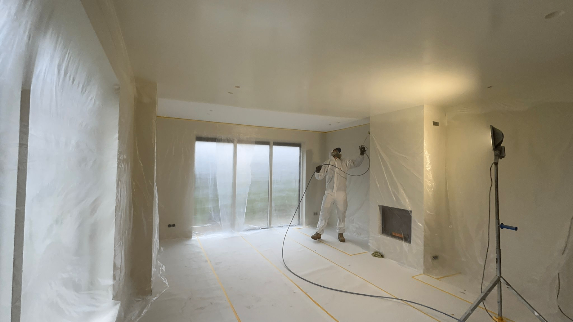 Vakman spuit latex op het plafond in een zorgvuldig afgeplakte woonkamer